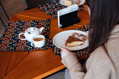 Bir kafede çayla bir dilim pastanın tadını çıkaran bir kadın..