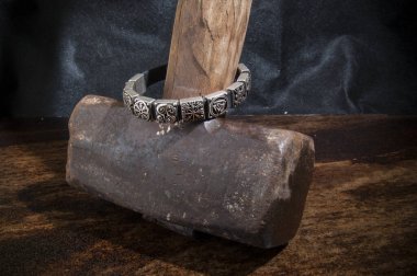 Üzerinde Viking sembolleri olan gümüş bir bileziğin yakın çekimi, ağır bir Thor 'un çekicinin üzerinde, koyu ahşap bir arka planda duruyor..