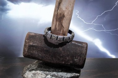 Üzerinde Viking sembolleri olan gümüş bir bileziğin yakın çekimi fırtınalı bir gökyüzüne karşı Thor 'un çekicinin üzerinde duruyor..