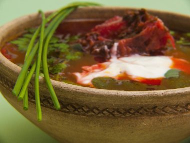 Orijinal bir kil kasede geleneksel borş çorbası yakın plan. Pancar, bitki ve ekşi krema gibi parlak malzemeler iştah açıcı bir görünüm yaratır..