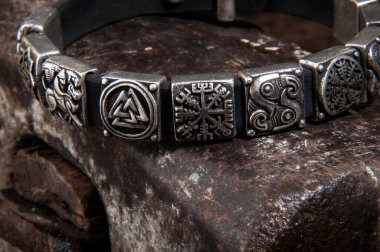 Metal plakalara İskandinav sembolleri işlenmiş büyük gümüş bir bileziğin detaylı görüntüsü. Kalıpların işçiliğine ve benzersizliğine odaklan..