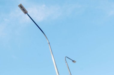 İki gösterişli LED sokak lambası açık mavi bir gökyüzüne karşı duruyor, modern, enerji tasarruflu kentsel aydınlanmayı simgeliyor. Temiz tasarım yeniliği vurguluyor.