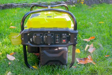 Çimlerin üzerinde sarı bir dönüştürücü jeneratörünün ön panelinin yakın çekimi. Soketler ve göstergeler görünür, çeşitli güç ihtiyaçları için işlevsellik ve hazırlık durumundadır.