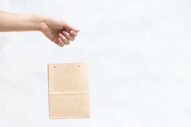 Hand of business woman hold brown paper shopping bag on white concrete background