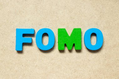 Color alphabet letter in word FOMO (abbreviation of fear of missing out) on wood background