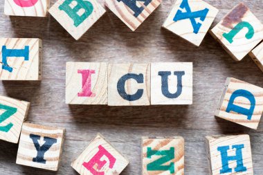 Alphabet letter block in word ICU (abbreviation of intensive care unit) and another letter on wood background