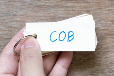 Hand hold flash card with handwriting in word COB (abbreviation of close of business) on wood background