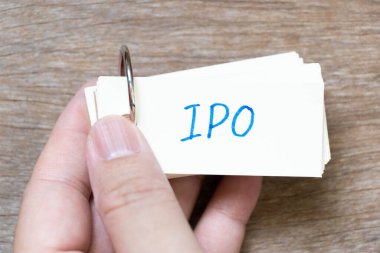 Hand hold flash card with handwriting in word IPO (Abbreviation of Initial Public Offering) on wood background