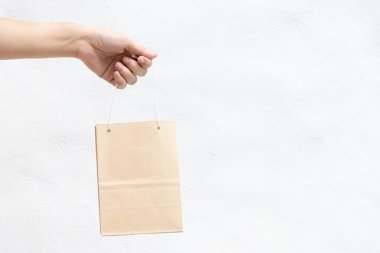 Hand of business woman hold brown paper shopping bag on white concrete background