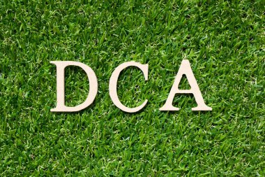 Kelime olarak tahta alfabesi harfi DCA (dolar maliyet ortalamasının kısaltması) yapay yeşil çimen arka planında