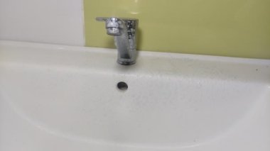 Temizlikçi, lavabo ve su musluğunu temizleyici ile yıkıyor.