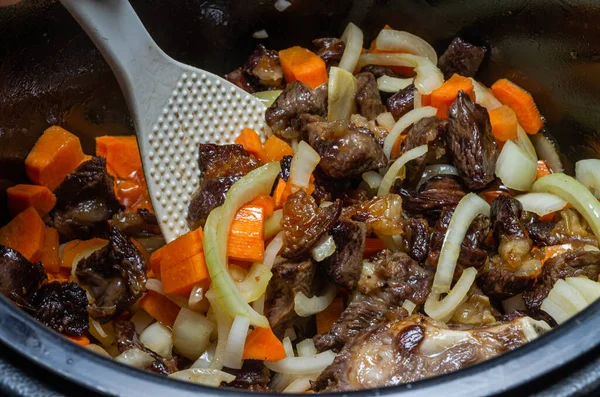 The cook fries lamb meat with onions and carrots in a multicooker pan