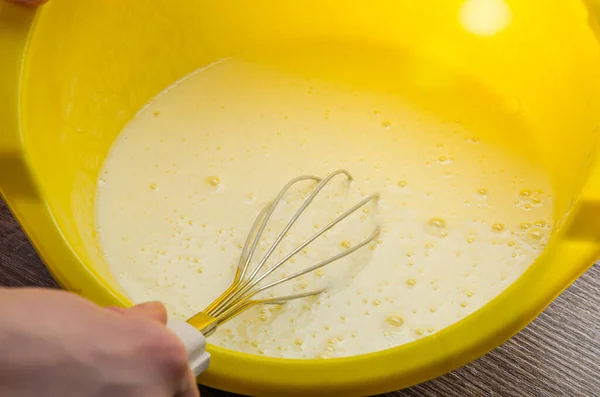 The cook beats the flour with a whisk into the dough for pancakes