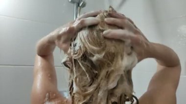 Genç ve güzel bir kız saçını şampuanla yıkıyor.