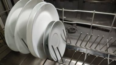 A man takes out clean dishes, white plates from the dishwasher