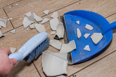 Bir hizmetçi kırık vazoyu süpürgeyle süpürür.