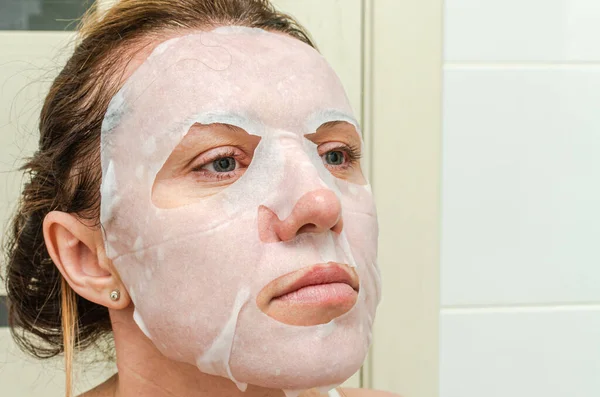 Young woman doing sheet mask on her face during beauty spa treatments