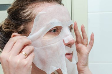 Güzellik tedavisinde yüzüne çarşaf maskesi takan genç bir kadın.