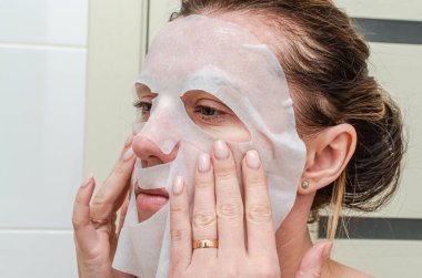 Güzellik tedavisinde yüzüne çarşaf maskesi takan genç bir kadın.