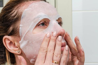 Güzellik tedavisinde yüzüne çarşaf maskesi takan genç bir kadın.