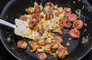 Aşçı tavada yumurta ve sosis kızartıyor.