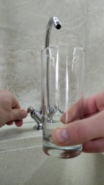 Dikey video. Bir adam musluktan bardağa su çeker.