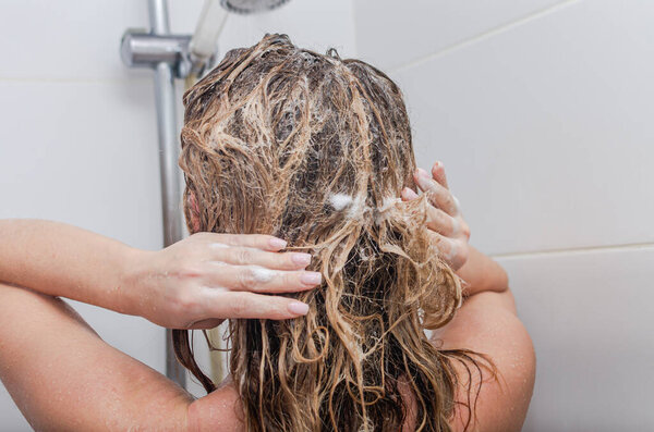 Young beautiful woman washing her hair with shampoo in the shower