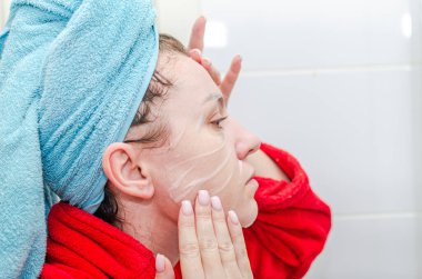 Bir kadın banyoda duş aldıktan sonra nemlendirici çarşaf maskesi takarak kendine spa güzellik tedavisi uyguluyor.