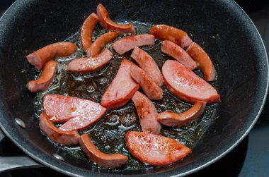 Kızarmış sosisler siyah arka planda kızartma tavasında.