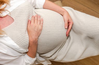 Beyaz elbiseli hamile kadın iki eliyle karnını tutuyor. Hamilelik ve gelecekteki annelik kavramı.