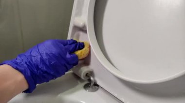 Temizlikçinin eldivenli eli tuvaleti temizler.