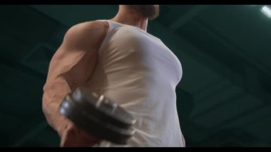 Güçlü adam, pazılar için sırayla halterlerle egzersiz yapıyor. Spor salonunun arka planında iyi fiziği olan genç bir adamın videosu. Kuvvet ve motivasyon.
