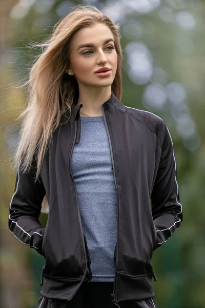A young woman with big lips and blue eyes looks away with her hands in the pockets of a black sports jacket. Beautiful woman looks away thoughtfully