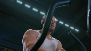 Sakallı, iri yapılı, kel, kaslı bir adam spor salonundaki bir ayak takımında kardiyo yapıyor. Odaklanmış bir atlet aşırı kiloları azaltmak için bir egzersiz yapar. Vücut yağını kardiyo ile azaltmak