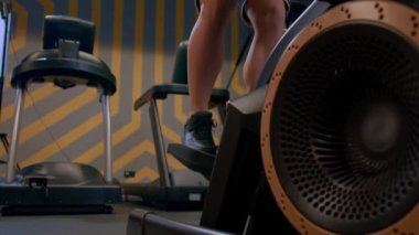 Kılsız kaslı erkek bacakları ritmik olarak kardiyo makinesine basıyor. Büyük baldır kasları. Kardiyodaki yüzü olmayan adam. Vücut yağını kardiyo ile azaltmak