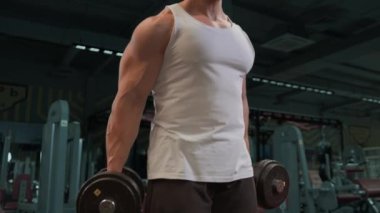 Güçlü adam, pazılar için sırayla halterlerle egzersiz yapıyor. Spor salonunun arka planında iyi fiziği olan genç bir adamın videosu. Kuvvet ve motivasyon.