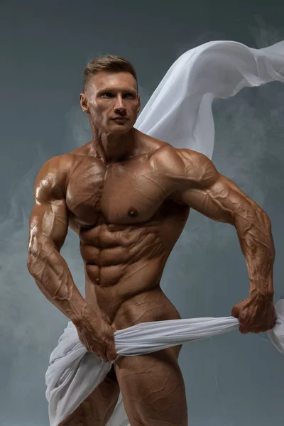 Aesthetics of the male athletic body. The male model covers the bottom of the torus with a white translucent fabric. 6 pack perfect abs