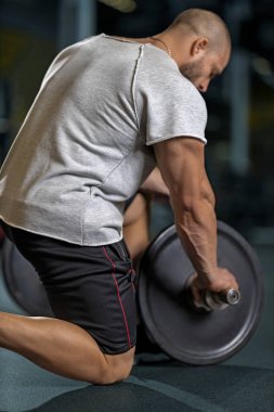 Güçlü kaslı bir adam halterin üstüne ağırlık koyuyor, genç, beyaz bir adam spor salonunda ağırlık kaldırmaya hazırlanıyor. Vücut geliştirme kavramı, boş alan