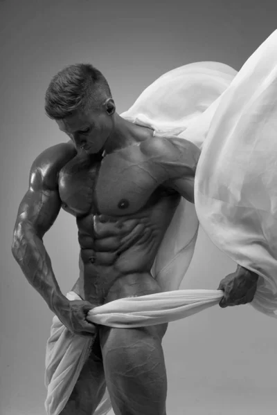 Aesthetics of the male athletic body. The male model covers the bottom of the torus with a white translucent fabric. 6 pack perfect abs. Black and white photo of a naked male athlete