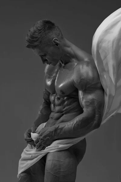 Aesthetics of the male athletic body. The male model covers the bottom of the torus with a white translucent fabric. 6 pack perfect abs. Black and white photo of a naked male athlete