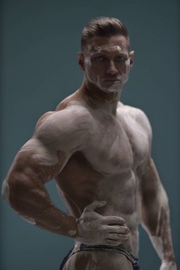 Mükemmel karın kasları olan güçlü kaslı bir adam stüdyoda boş bir arkaplanda poz veriyor. Atletik erkek vücudu antika bir heykel şeklinde beyaz kille kaplıdır.