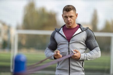 Handsome athletic man exercising with resistance band outdoors in the sun