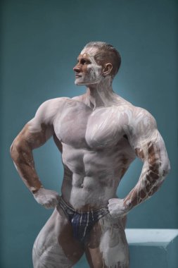 Kaslı bir adamın stüdyo fotoğrafı. Gri arka planda çıplak bir şekilde poz verirken güzel çıplak gövdesi olan yakışıklı, beyaz tenli bir adam. Spor antrenmanı konsepti
