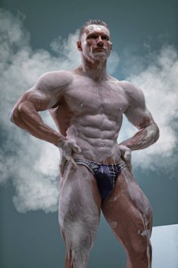 Kaslı bir adamın stüdyo fotoğrafı. Gri arka planda çıplak bir şekilde poz verirken güzel çıplak gövdesi olan yakışıklı, beyaz tenli bir adam. Spor antrenmanı konsepti