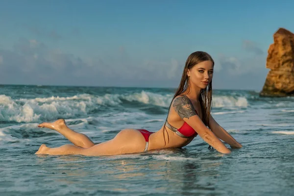 身穿比基尼 头戴丁字裤的性感女人 在海滨度假期间的海浪中 躺在海滩沙滩上的沙滩上 晒黑了皮肤 抬起了脚 海滩上的夏日美景 — 图库照片