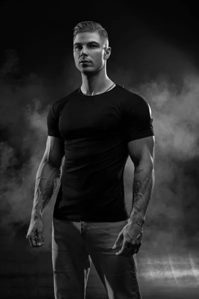肌肉发达的模特是穿着牛仔裤和黑色背景T恤的年轻人 时尚肖像画的野蛮的运动健康强壮的肌肉家伙与现代流行的发型 黑白照片 — 图库照片