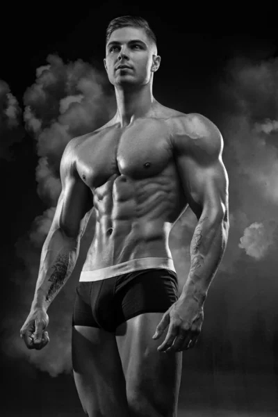 身材魁梧的成年肌肉男模特儿在黑色背景的短裤上摆姿势 显示出完美的腹肌 黑色和白色照片的比例较低 — 图库照片