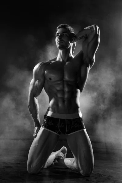 力強い陸上競技の男は黒のスタジオで膝の上に恥知らずな立ちポーズ 6パック腹筋と脂肪黒と白の写真の低い割合を持つ運動筋体 — ストック写真