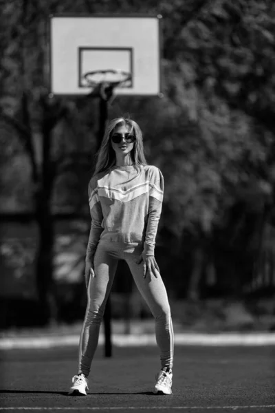 身穿白黑色运动服的金发女运动员站在篮球场上 — 图库照片