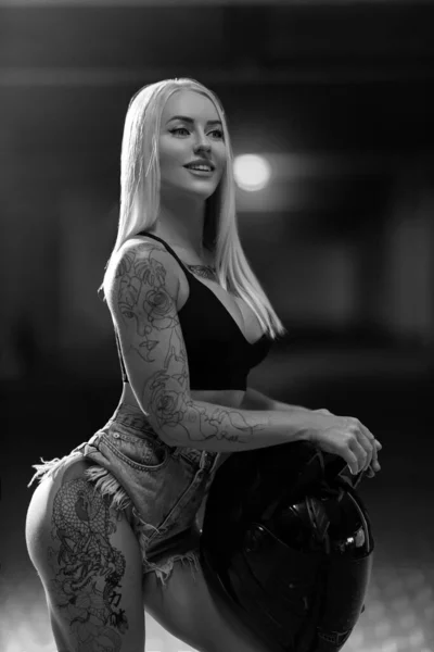 性感的金发女人模特 胸部是硅胶的 手上拿着摩托车头盔 手拿着黑白照片 — 图库照片